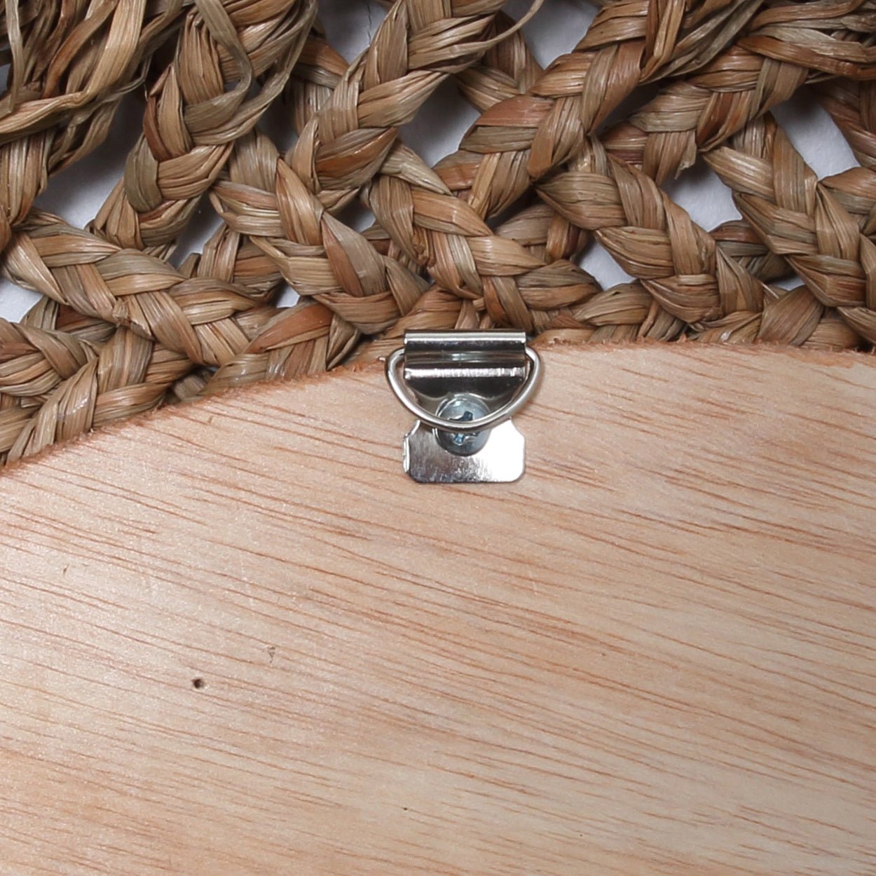 Gevlochten rieten mat bovenaan en metalen haak op hout voor wandmontage, rustieke uitstraling.