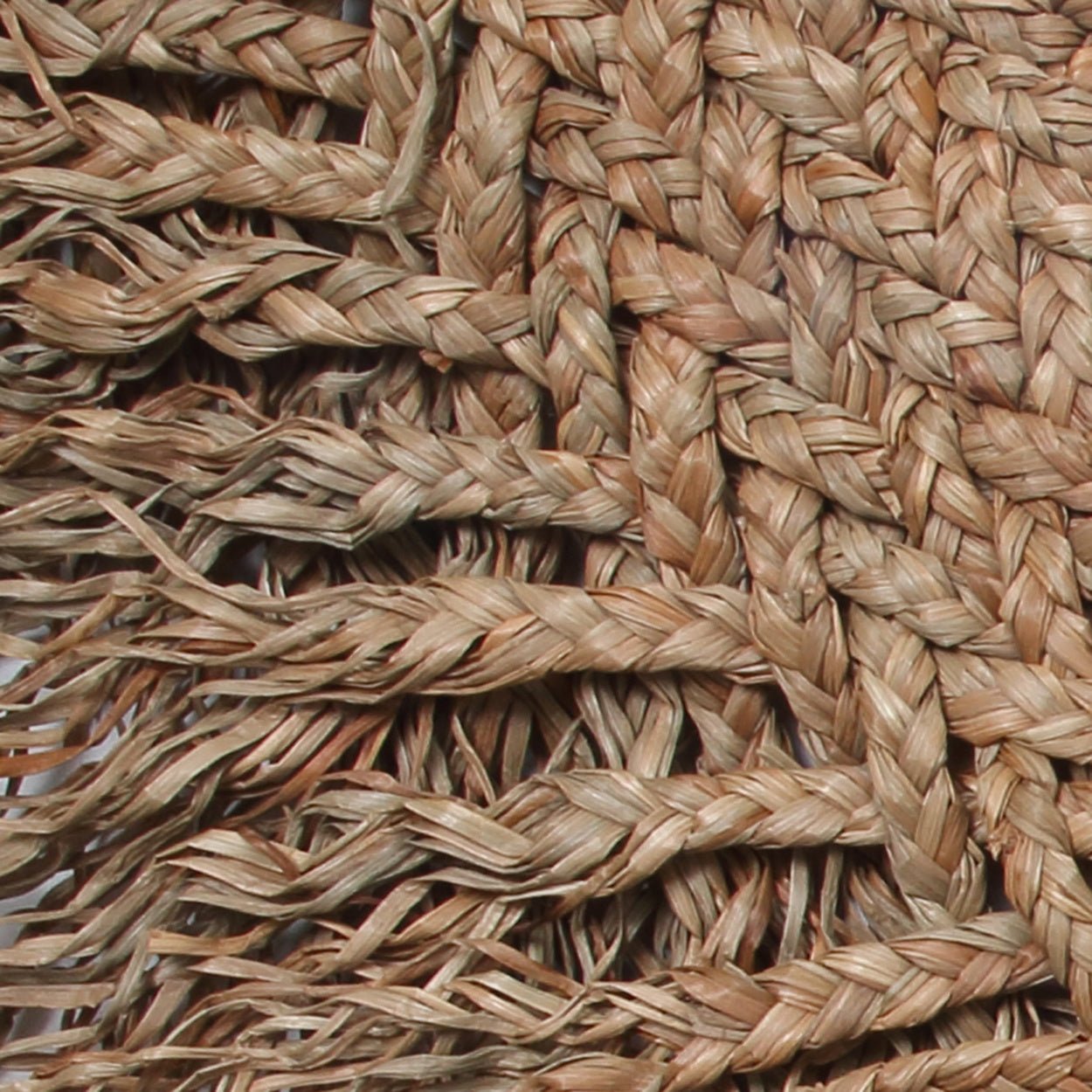 Gevlochten jute vloerkleed met een patroon van natuurlijke vezels en losse franjes aan de rand.