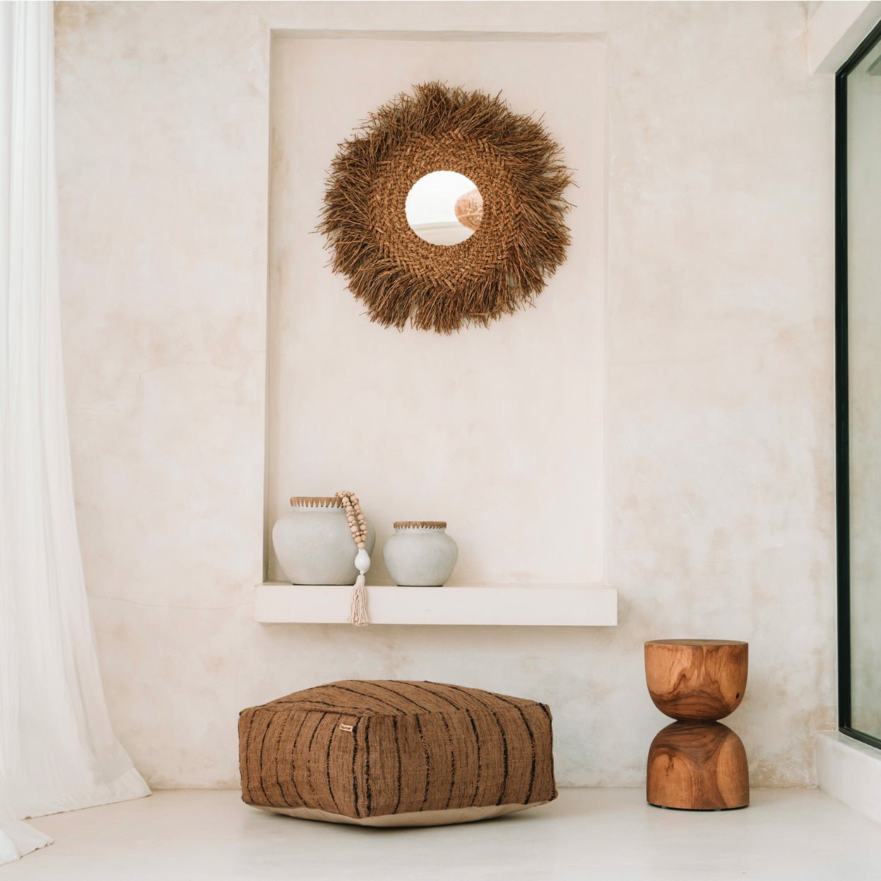 Stijlvol interieur met een rieten spiegel, houten kruk en beige accessoires op een lichte marmeren vloer.