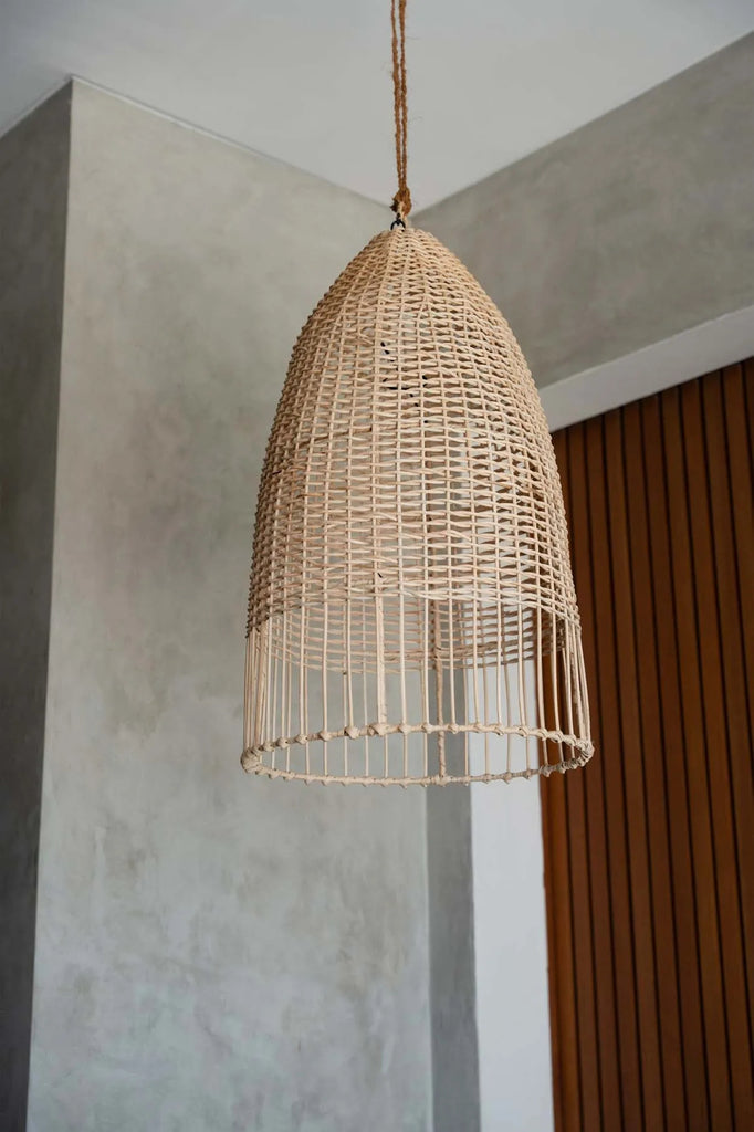 Hanglamp van natuurlijk riet met gebogen vorm, hangend aan plafond met grijze betonnen muur als achtergrond.