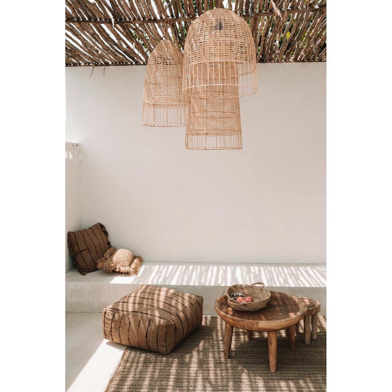 Zonnige bohemian zithoek met rieten lampen, houten tafel en kussens, omringd door lichte schaduwen.