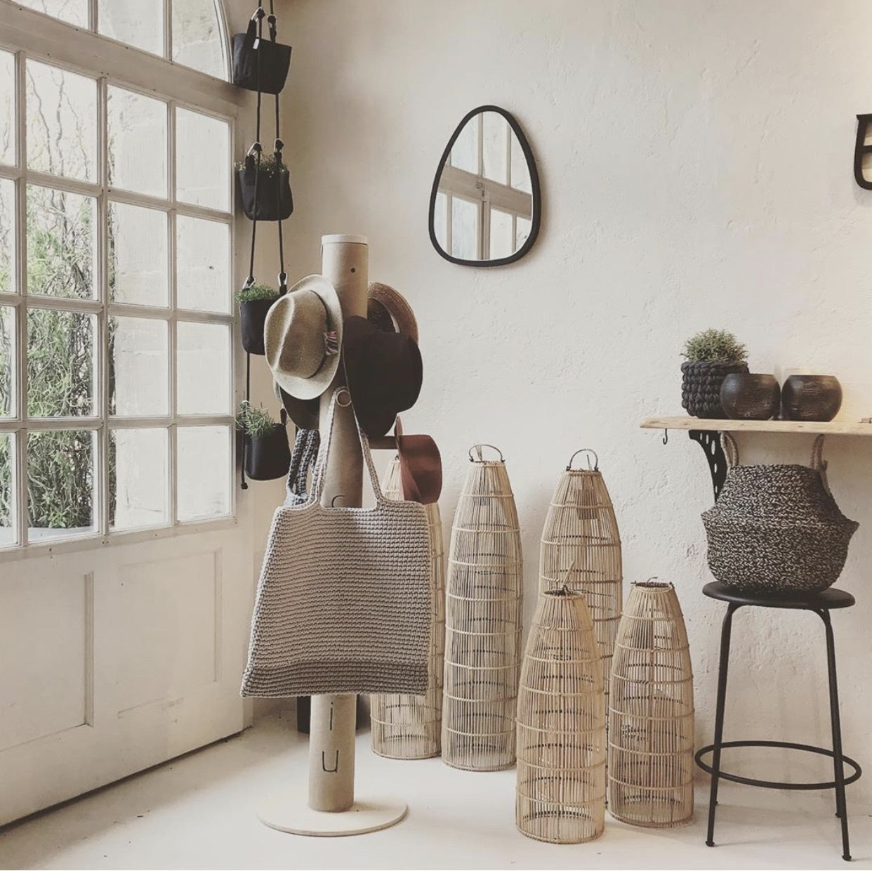 Stijlvolle kamer met hoeden, geweven tas, rieten manden en een spiegel op beige muur, serene sfeer.