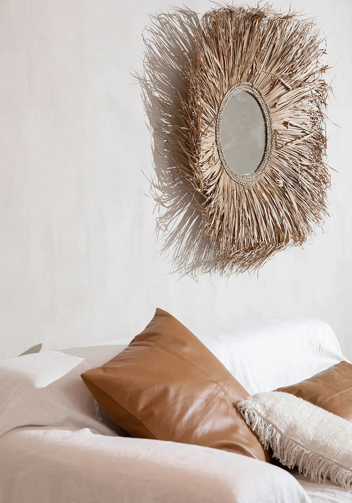 Bruine rotan spiegel en witte stoffen bank met bruine leren en beige geweven kussens in een lichte kamer.