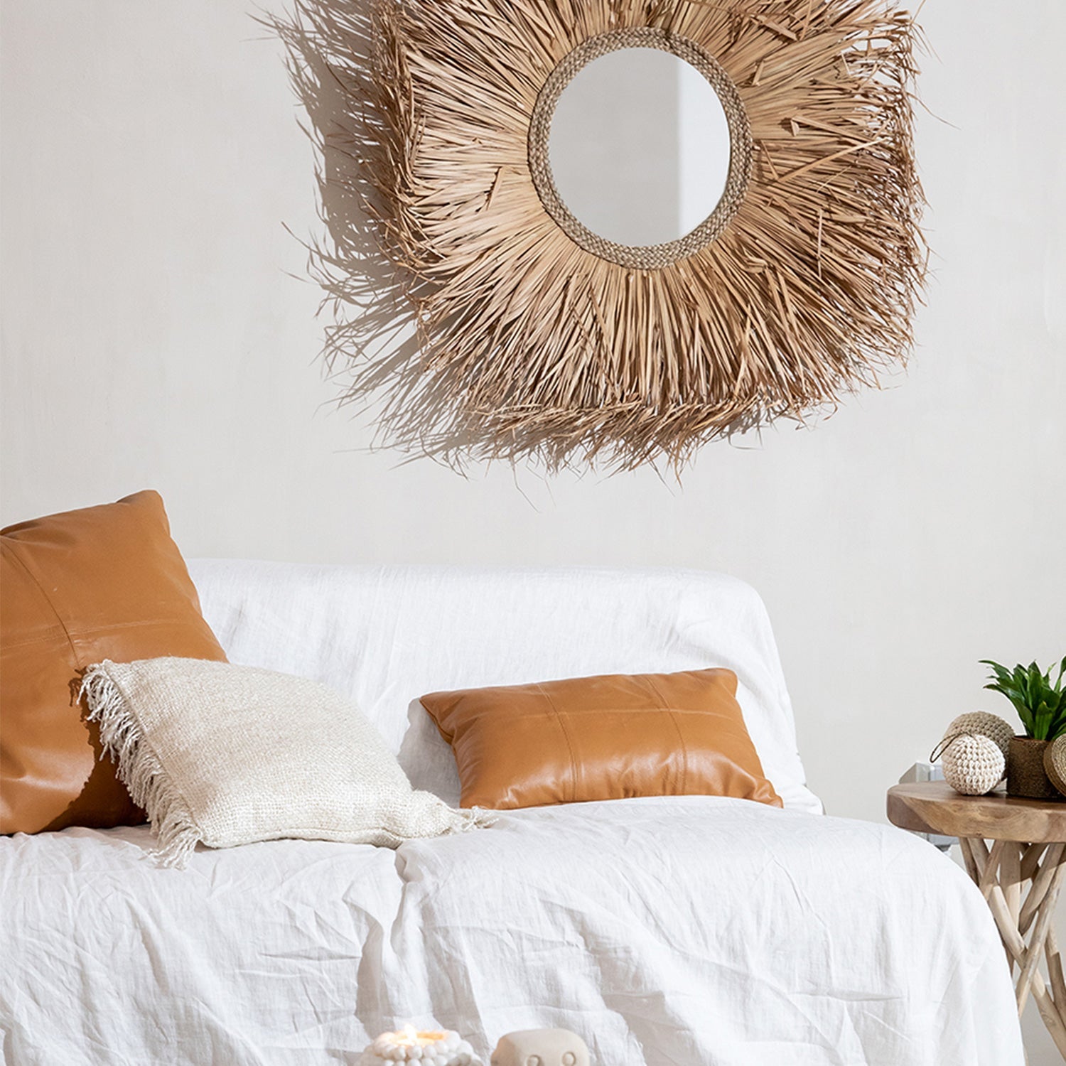 Woonkamer met rotan spiegel, witte bank met bruine kussens en bijzettafel met planten voor ontspanning.