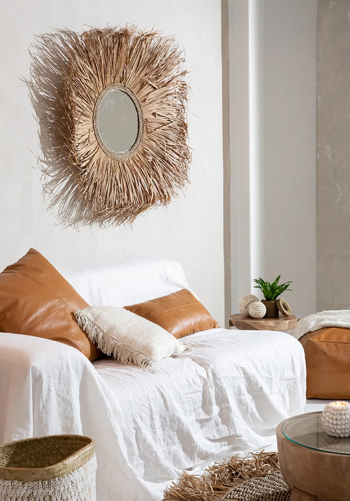 Natuurlijke woonkamer met een rotan spiegel, witte bank met bruine kussens, en een houten bijzettafel met plant.