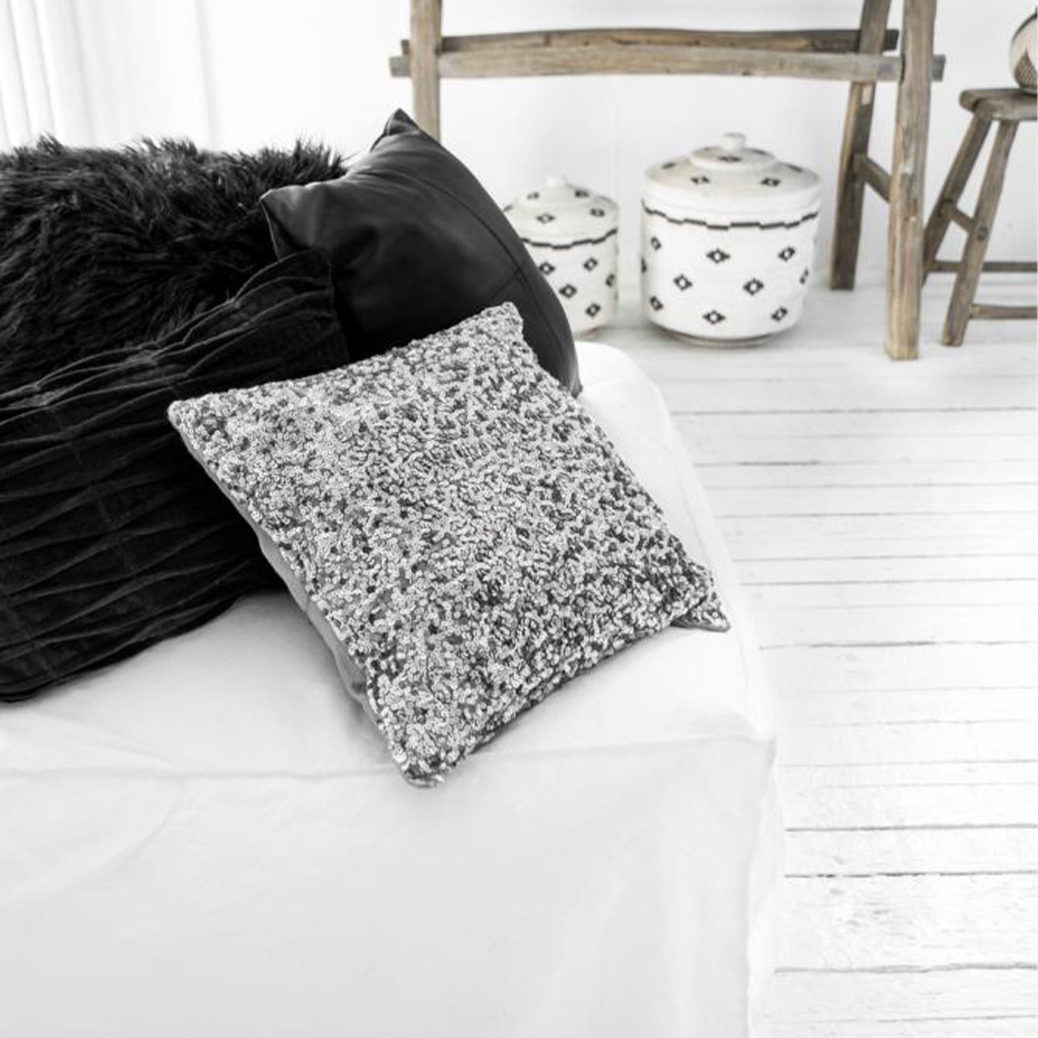 Zwart-wit interieur met sierkussens op een bank, geleefde houten vloer en decoratieve opbergmanden.