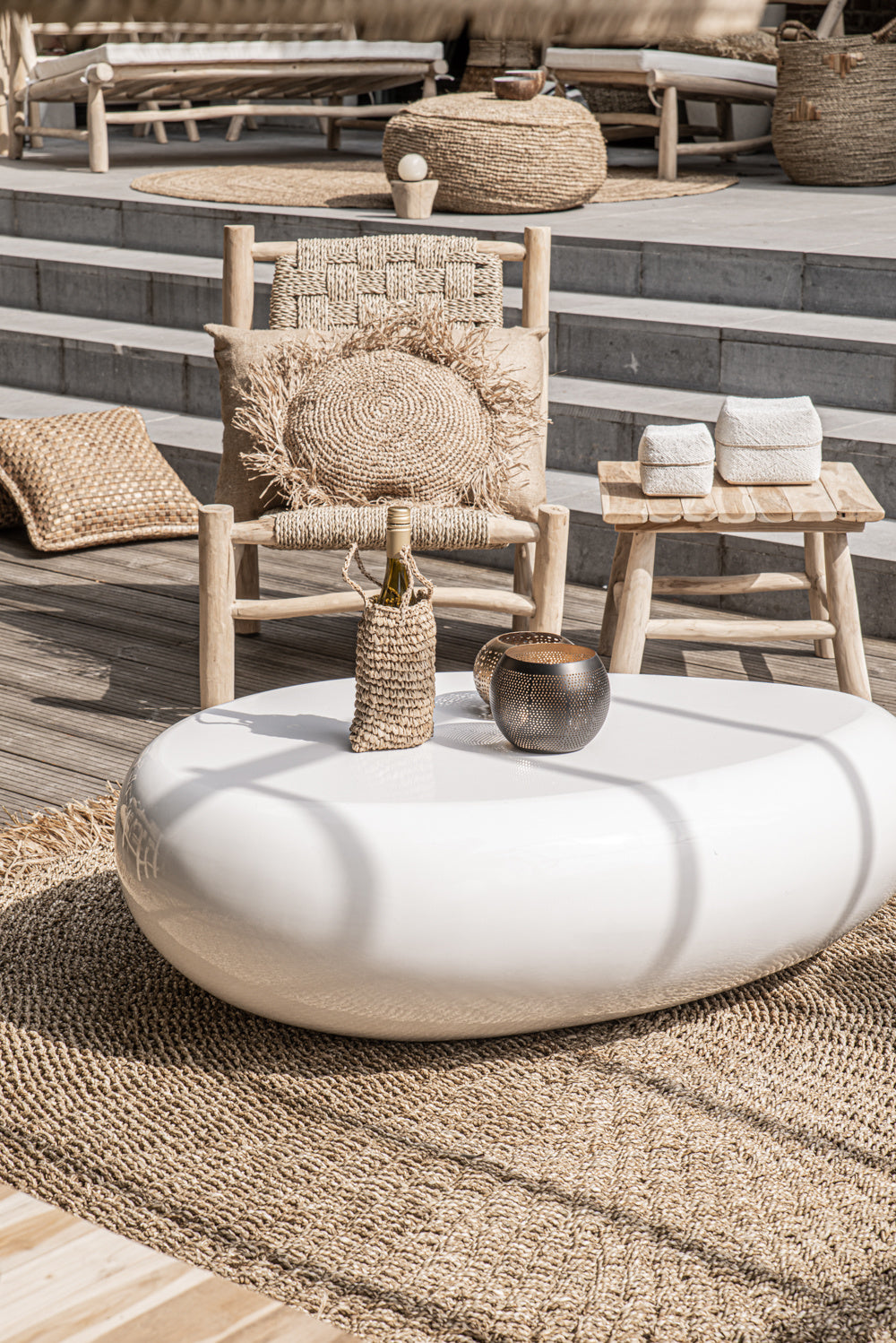 Moderne buitenruimte met houten meubels, rotan decor en witte ovale tafel op een gevlochten kleed.