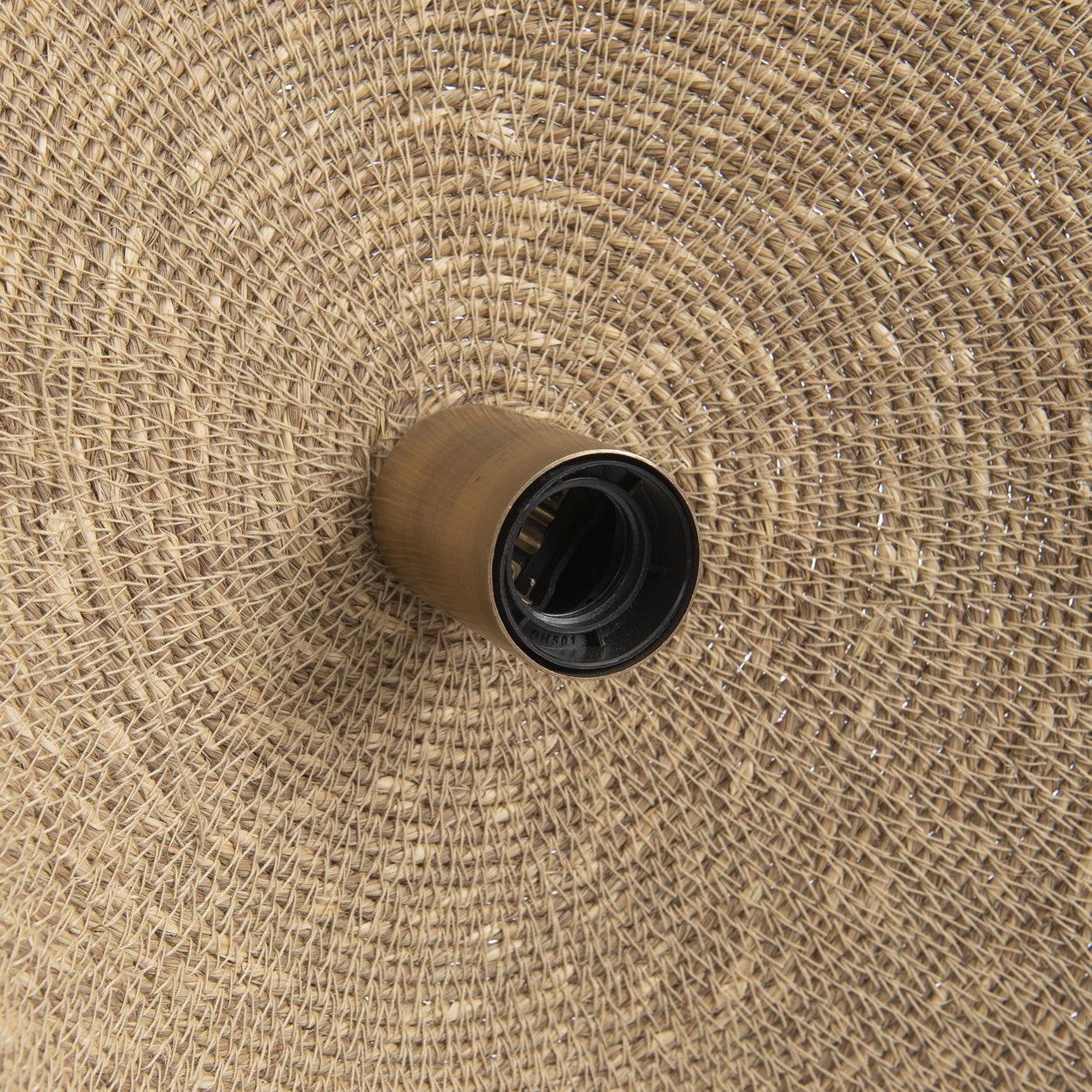 Een lamp met een messing fitting op een geweven rotan achtergrond, cirkelvormig patroon.