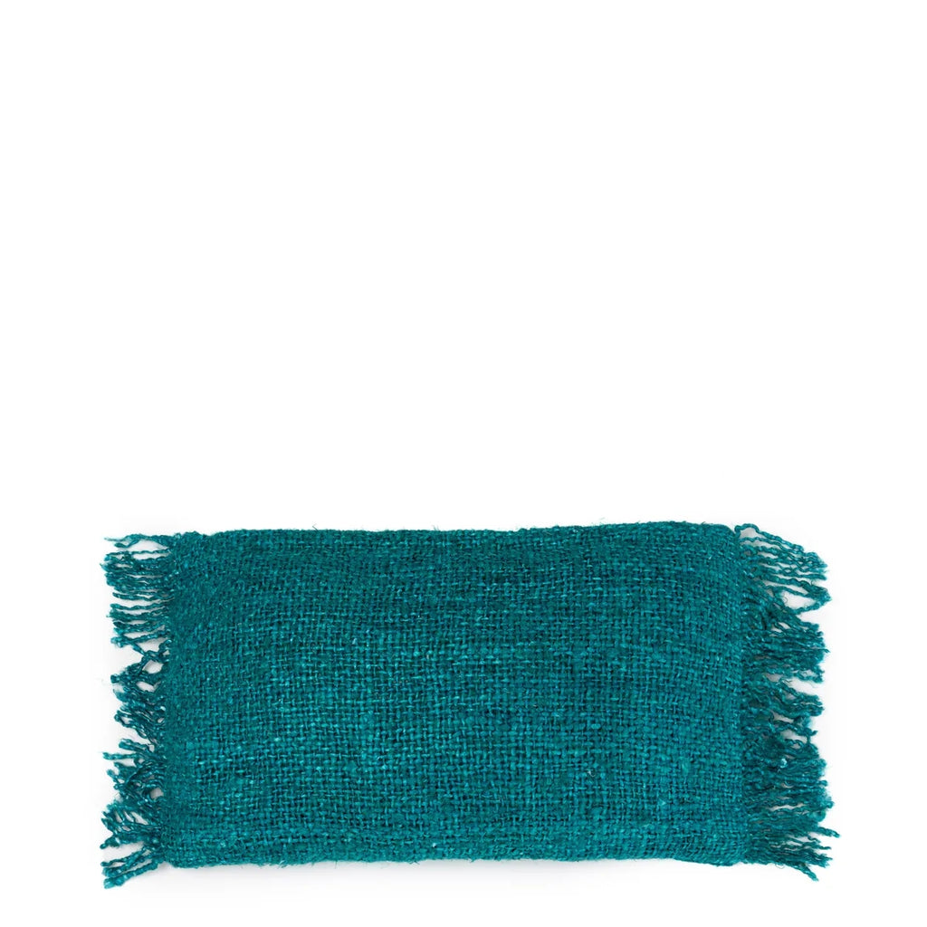 Turquoise rechthoekig kussen met franjes op heldere witte achtergrond, geweven textuur zichtbaar.
