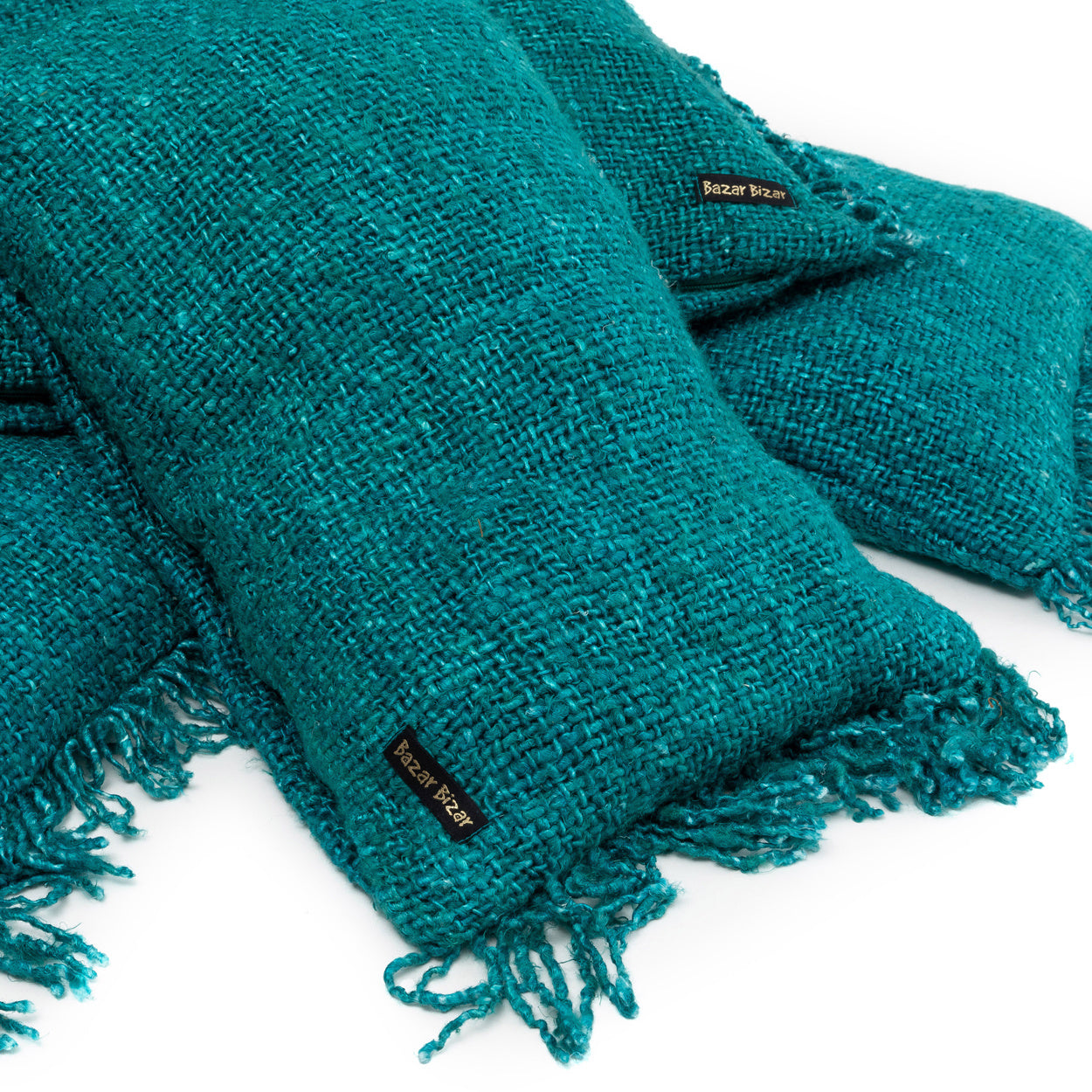 Turquoise geweven kussens met franjes, label "Bazar Bizar", op een witte achtergrond geplaatst.