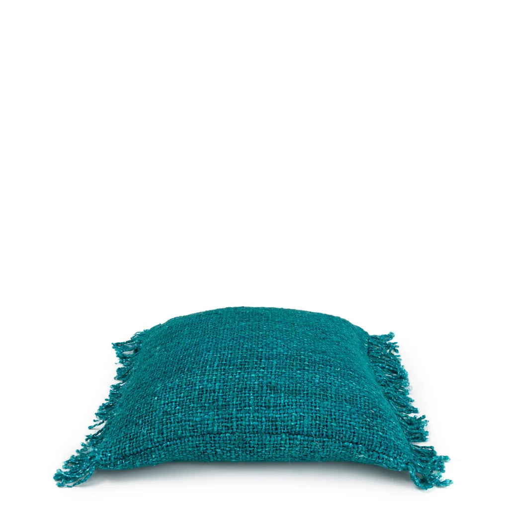 Turquoise geweven kussen met franjes, elegant geplaatst op een witte achtergrond.