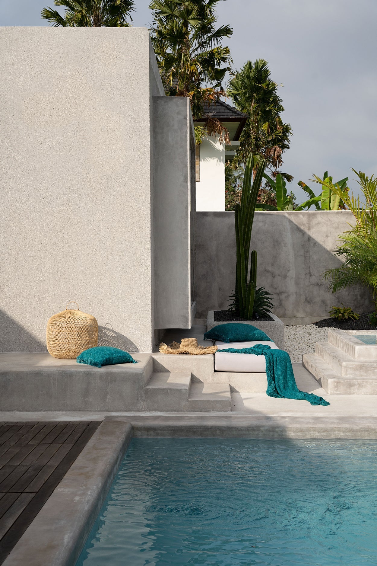 Moderne zwembad met serene loungehoek, turquoise kussens, hoed en rieten mand, omgeven door palmbomen.