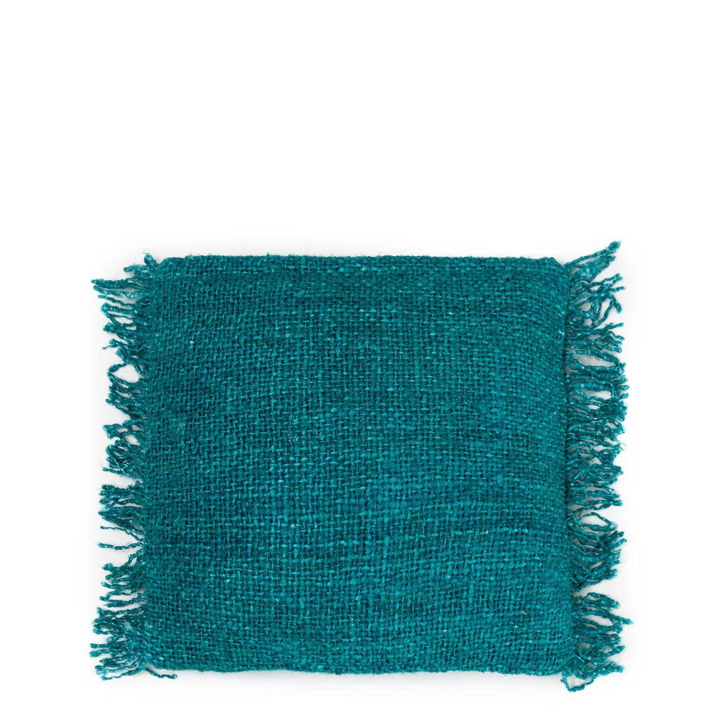 Vierkant turquoise kussen met een ruwe textuur en franjes aan de randen, geïsoleerd tegen witte achtergrond.