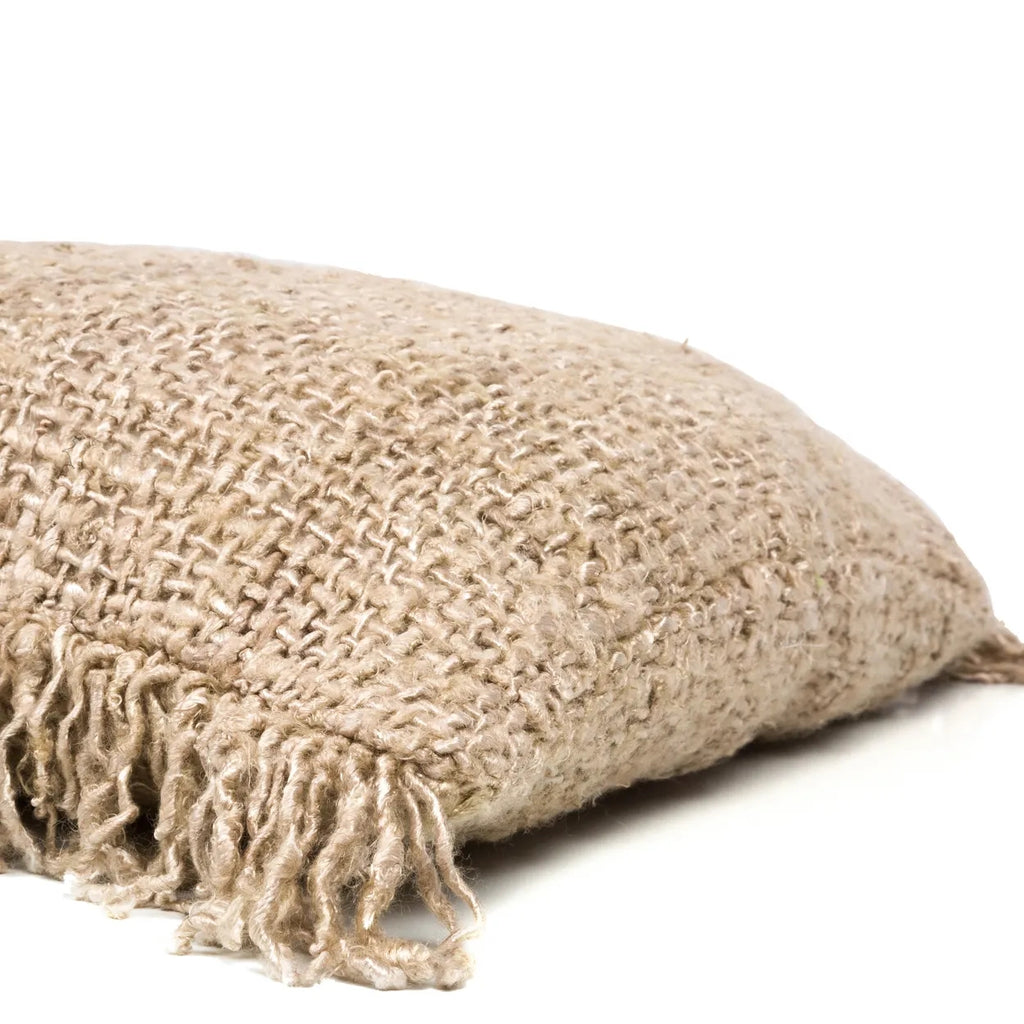 Beige jute kussen met een grove textuur en franjes aan de rand, liggend op een witte achtergrond.