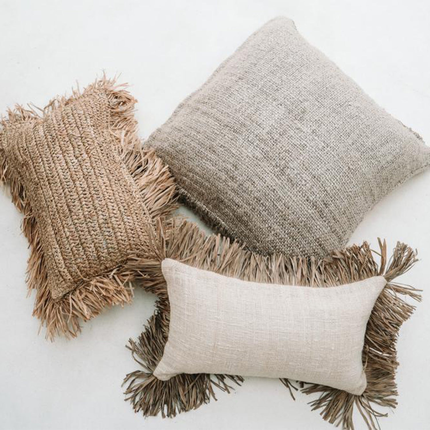 Drie decoratieve kussens met franjes; natuurlijk geweven materialen in beige en lichtbruin tinten.