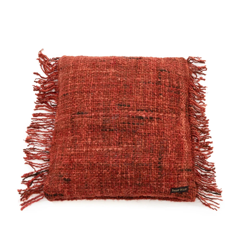 Rood, vierkant kussen met ruw textiel en franjes. Leren label met tekst "Bazar Bizar" aan de zijkant.