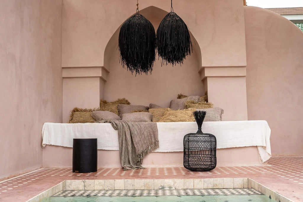 Stijlvolle loungehoek met beige kussens en zwarte lampen, gelegen bij een mozaïekzwembad op een roze patio.