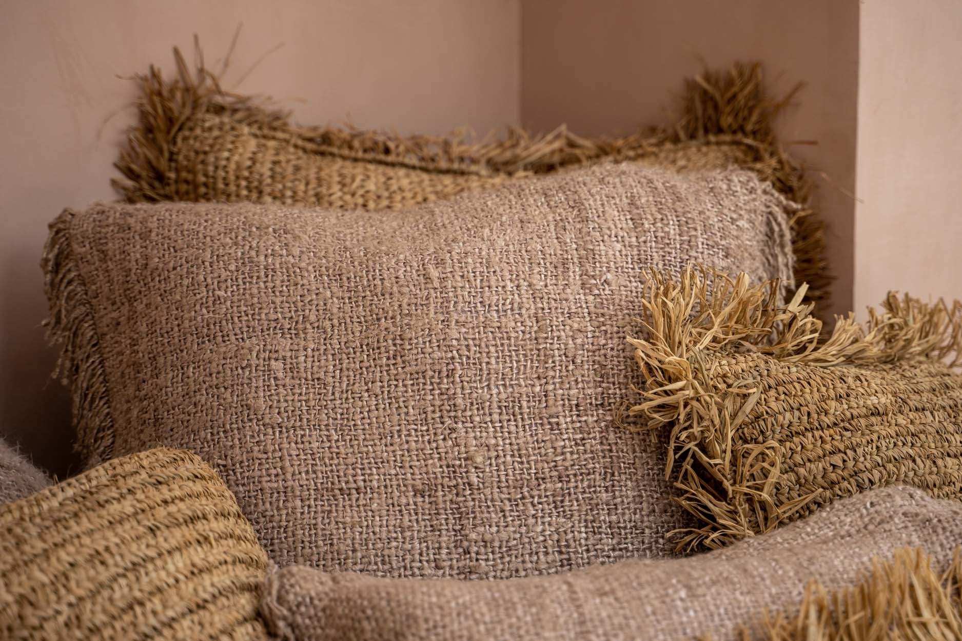 Stapel sfeervolle, neutrale juten kussens met ruwe textuur en decoratieve randjes in een hoek.
