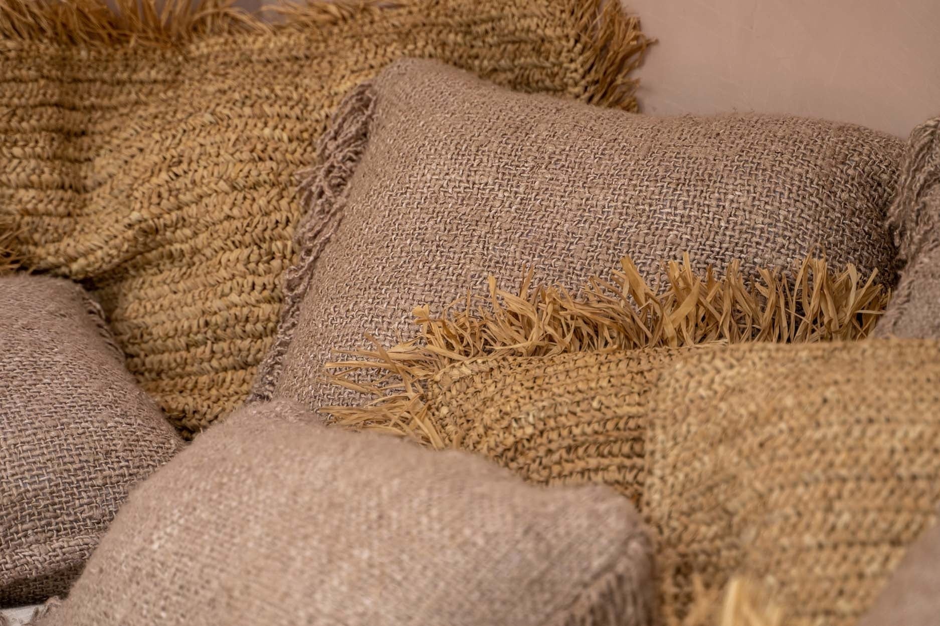 Natuurlijke jute kussens met beige tinten en decoratieve franjes, stijlvol gegroepeerd op een bank.