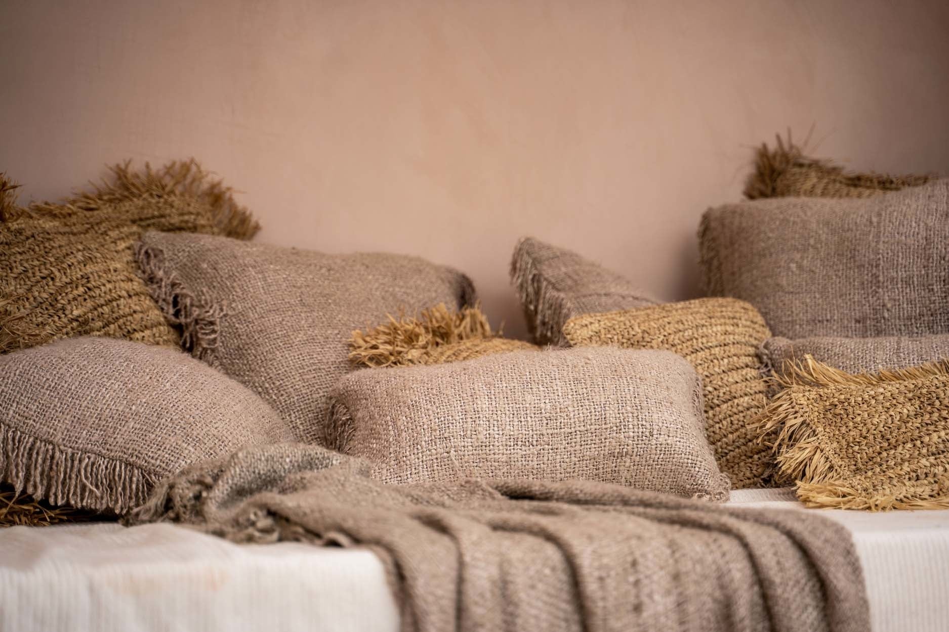 Gezellige bank met beige jute kussens en plaids, benadrukt een rustieke en warme sfeer in de kamer.