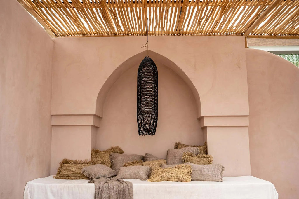 Rustieke loungehoek met aardetinten kussens, een geweven hanglamp en een bamboe dak voor een serene sfeer.