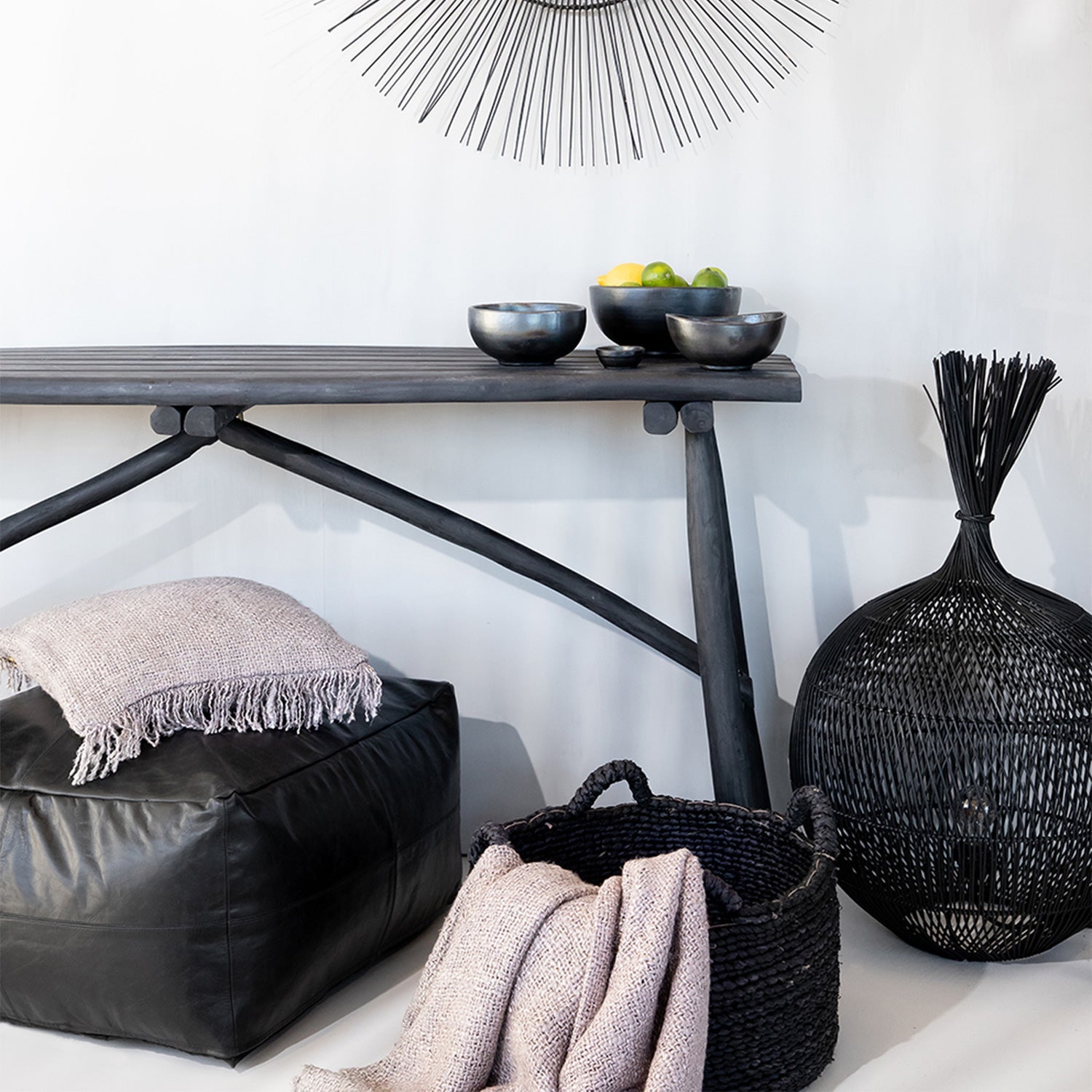 Chique zwart interieur met houten tafel en schaal met fruit, leren poef en mand met deken, minimalistisch ontwerp.