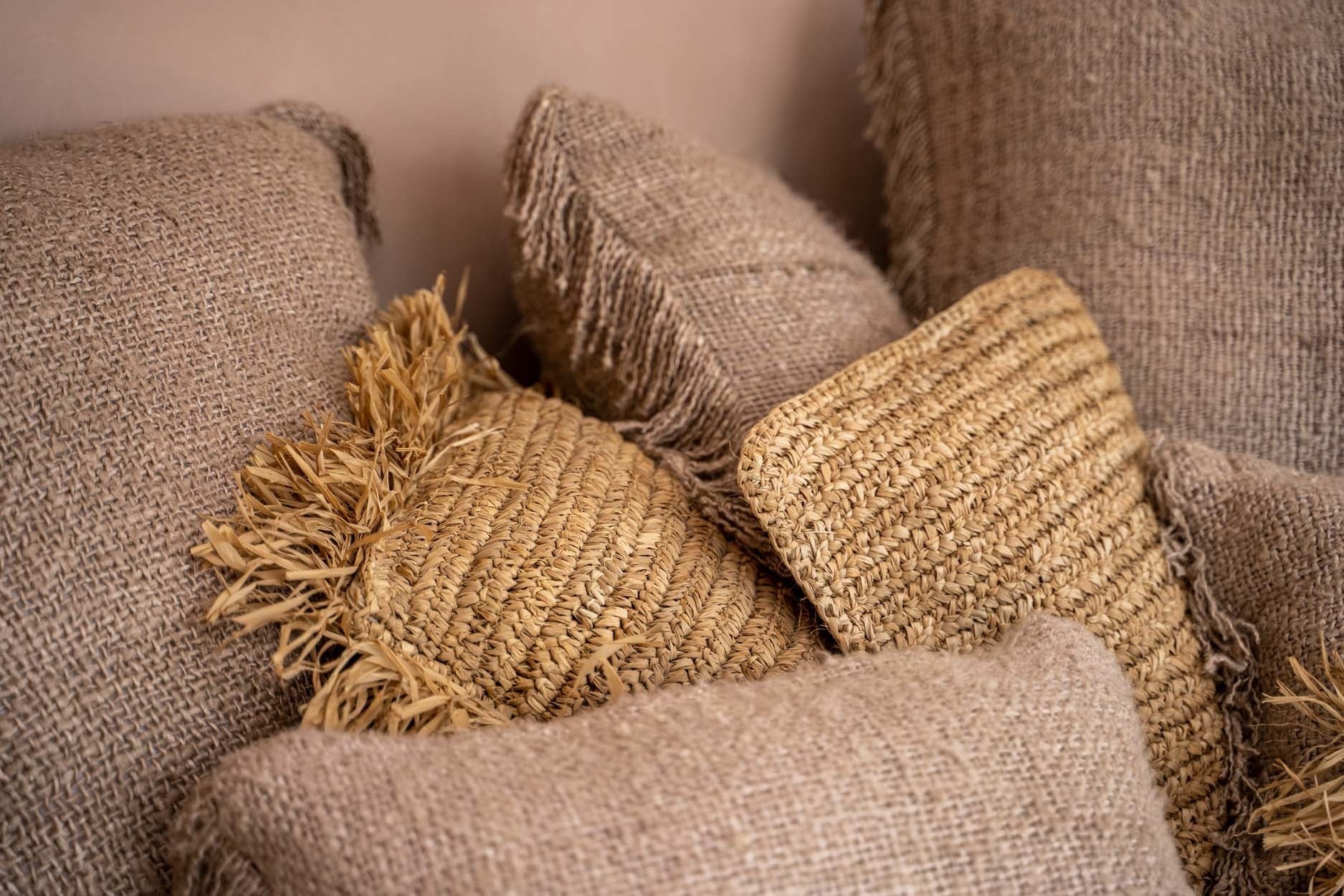 Stapel van rustieke kussens met jute en gevlochten riet, textuurrijk en sfeervol in natuurlijke tinten.