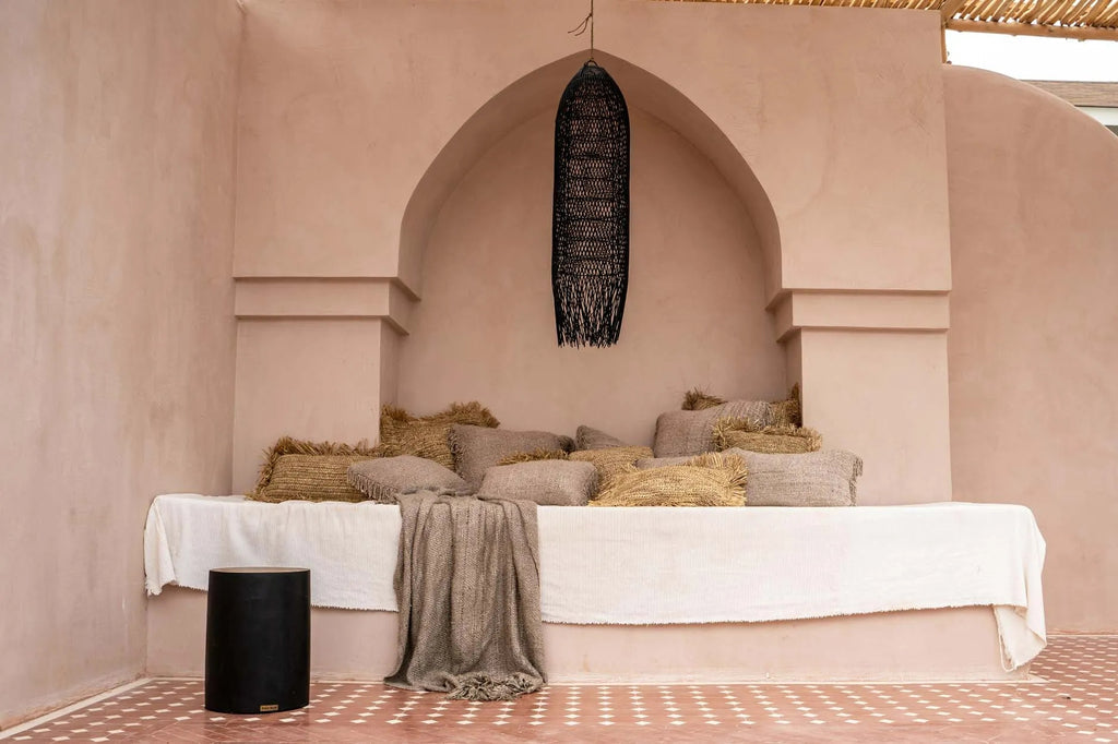Sfeervol beige interieur met gestapelde kussens en een hanglamp, rustieke texturen en een rustige ambiance.
