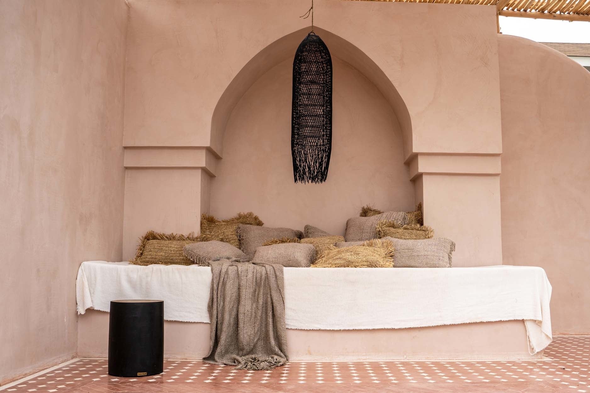 Knusse beige nis met kussens en dekens, zwart geweven hanglamp, gezellige ontspanningssfeer.