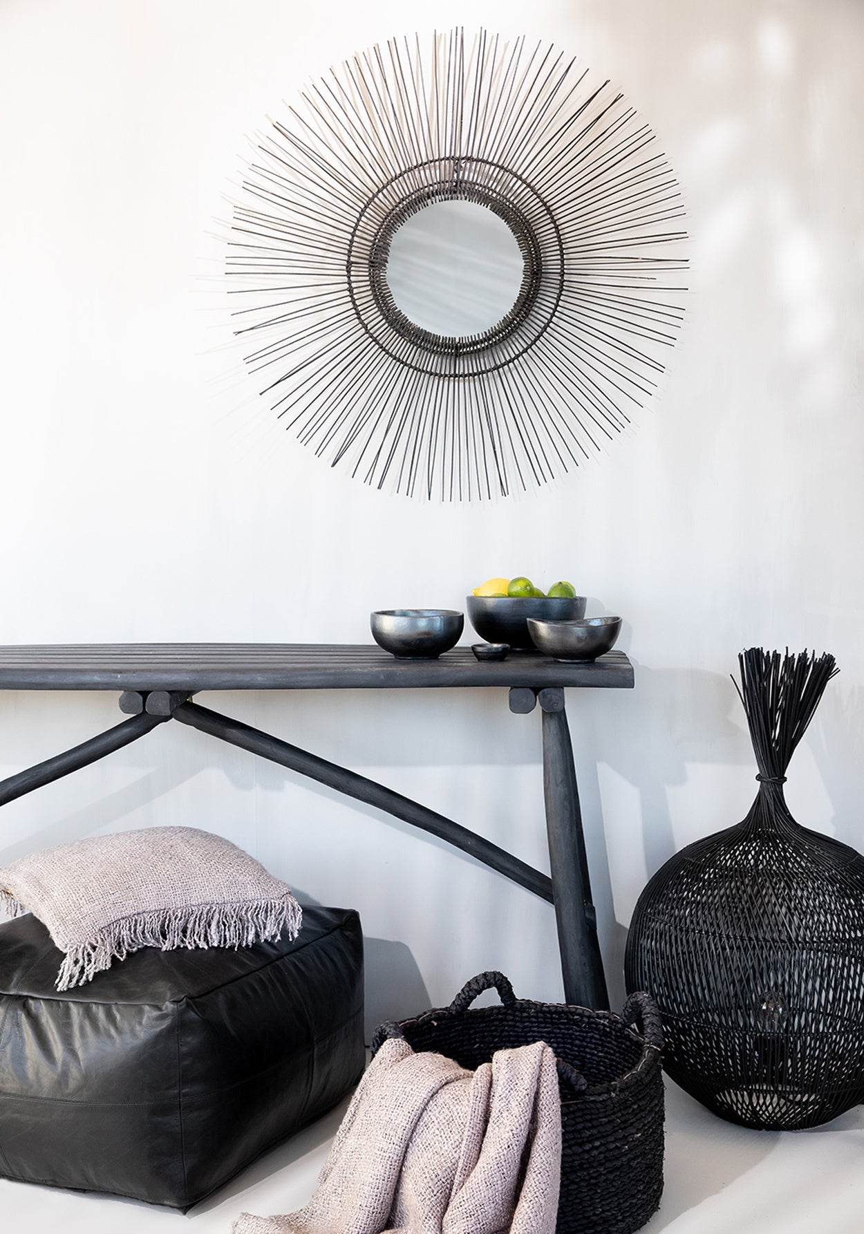 Sfeerhoek met decoratieve spiegel, zwarte tafel met kommen, en zachte dekens in een mand, strakke witte muren.