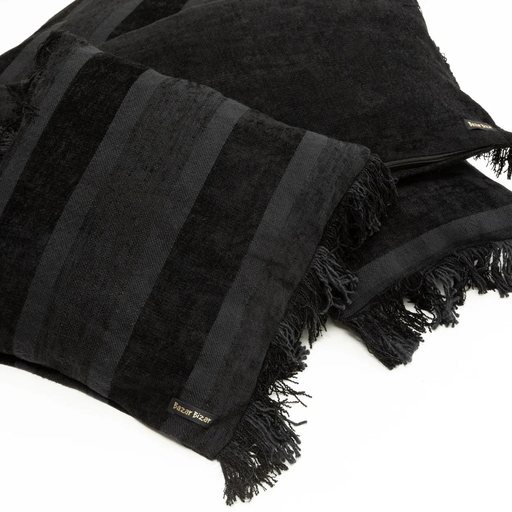 Zwarte kussens met franjes en subtiele strepen, label "Bazar Bizar" zichtbaar, elegante woonaccessoires.