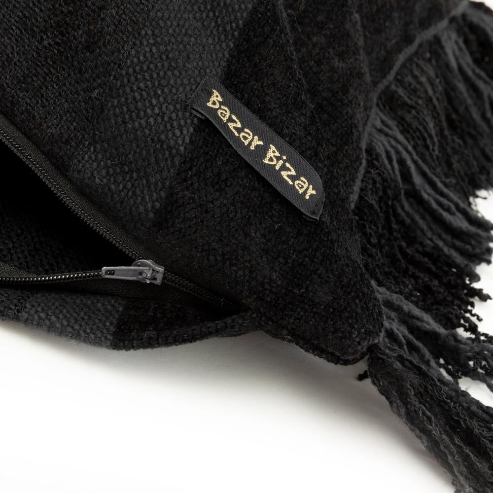 Zwarte plaid met franjes en ritssluiting, label met "Bazar Bizar". Zacht en stijlvol ontwerp.