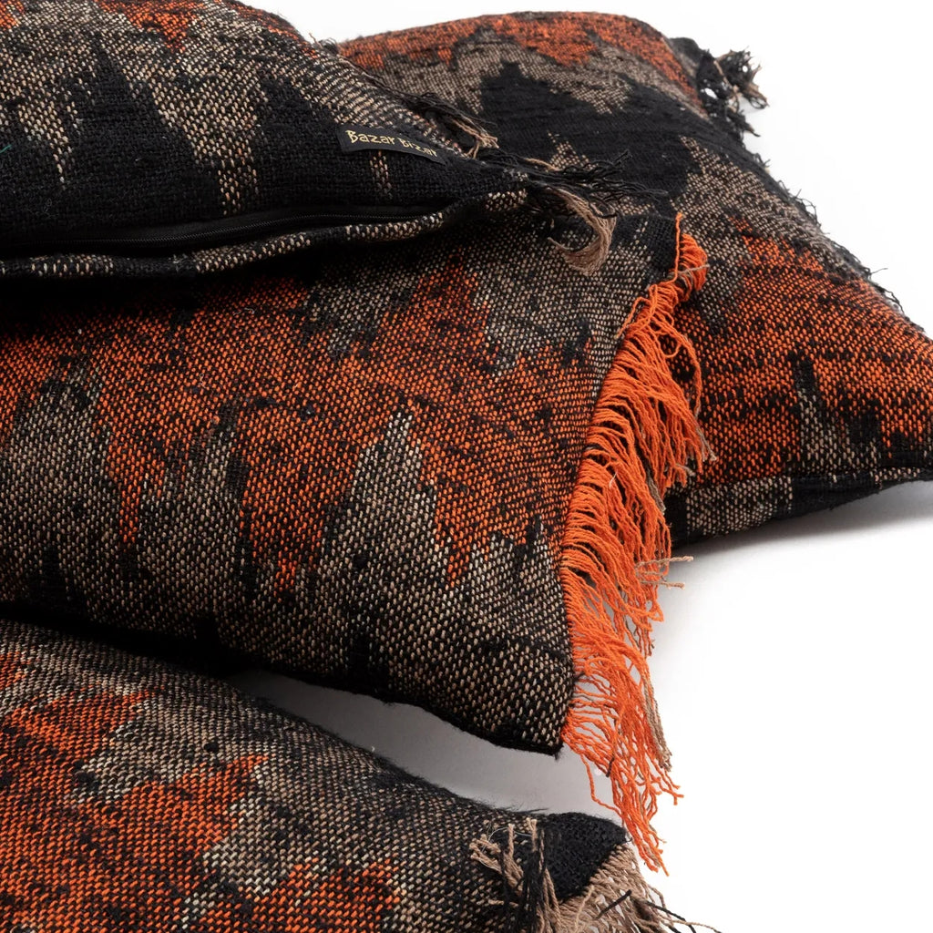 Zwart en oranje kussens met rafels, met een borduurlabel "Bazar Bizar" zichtbaar.