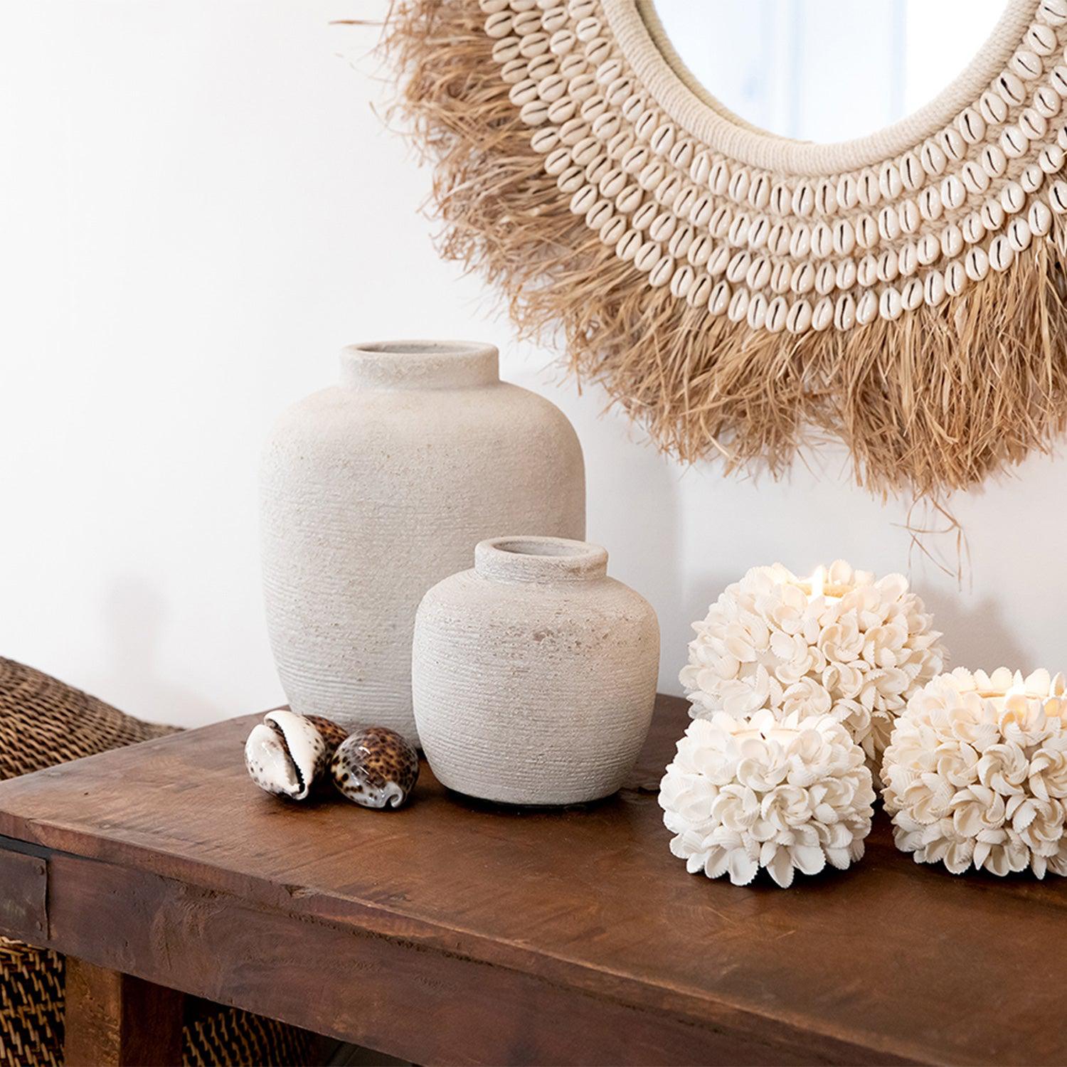 Rustieke vazen en schelpenkaarsen op houten tafel, met decoratieve spiegel met schelpen en stro.