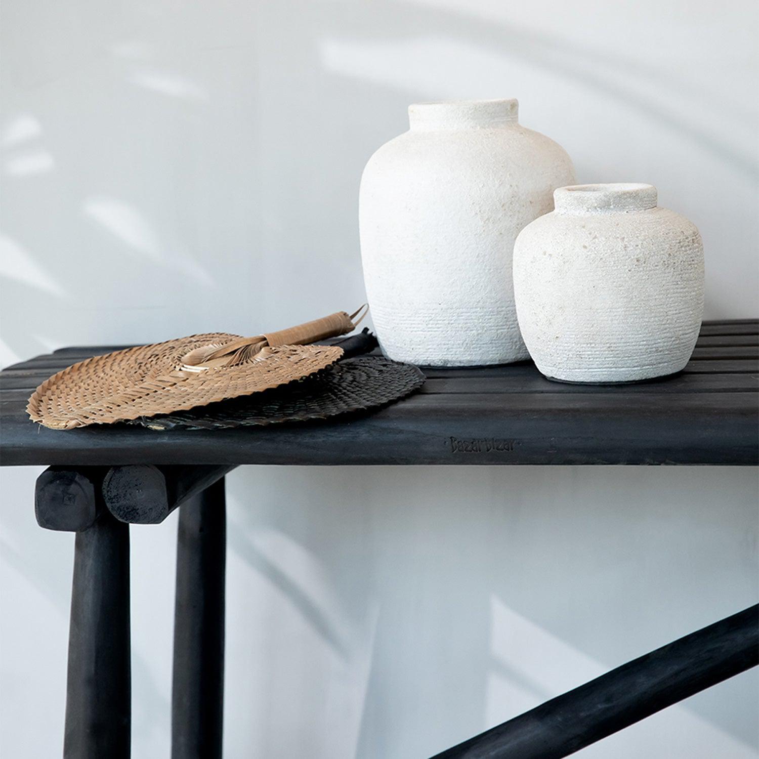 Twee witte vazen en rieten waaiers op een zwart houten tafel, minimalistische en rustieke esthetiek.