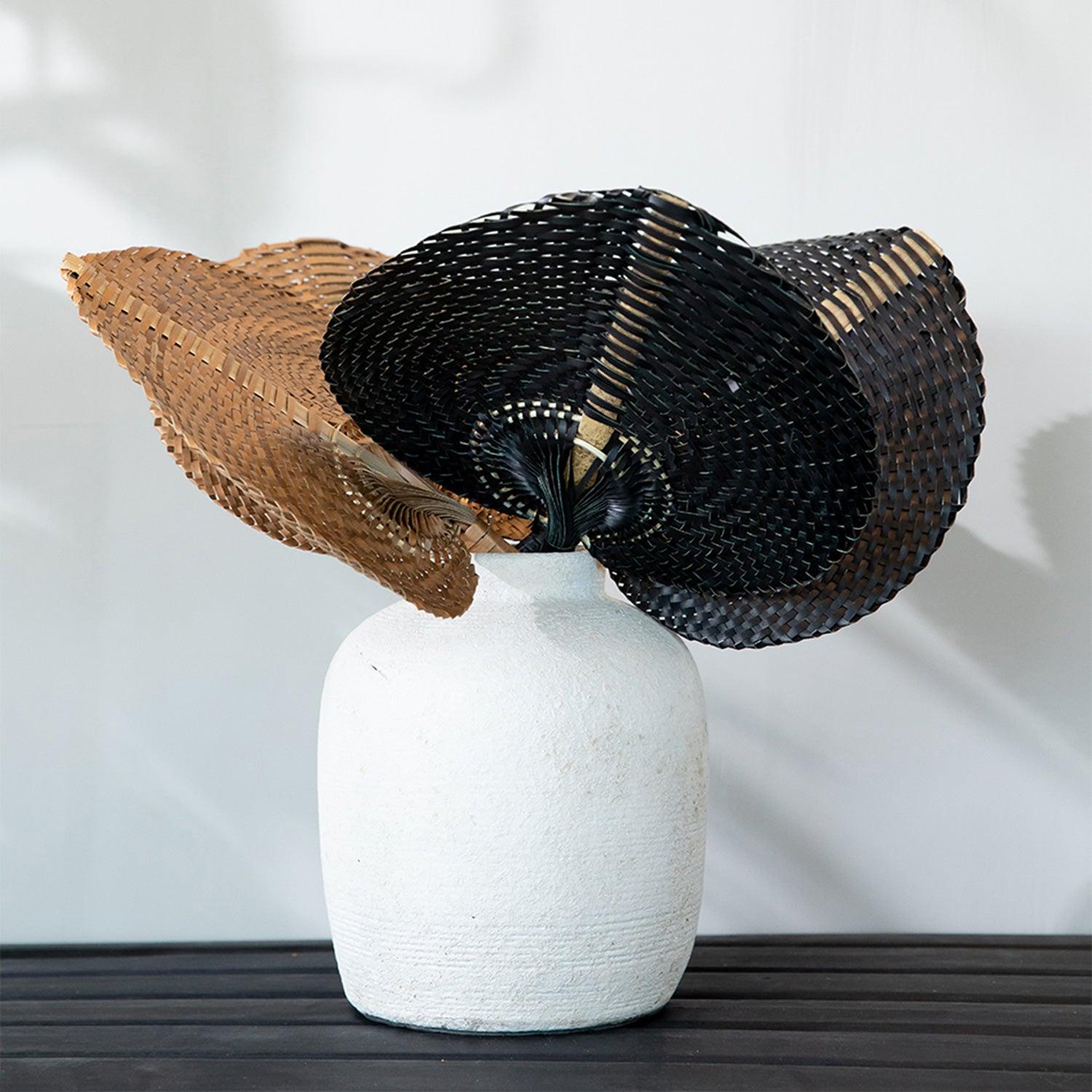 Witte vaas met twee decoratieve waaierachtige manden, één bruin en één zwart, op een donker houten tafel.