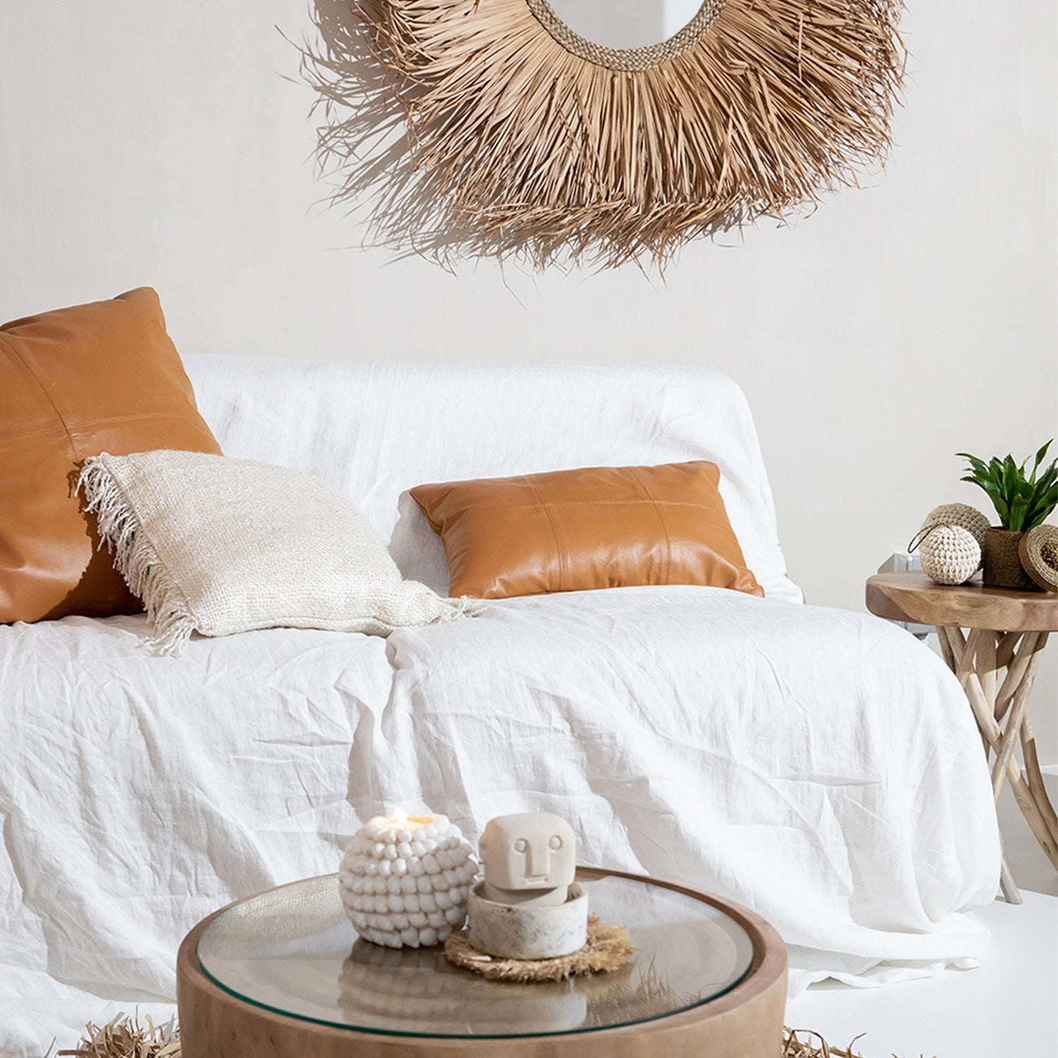 Witte bank met bruine kussens, rotan spiegel, klein tafeltje met planten en een decoratieve kaars op tafel.