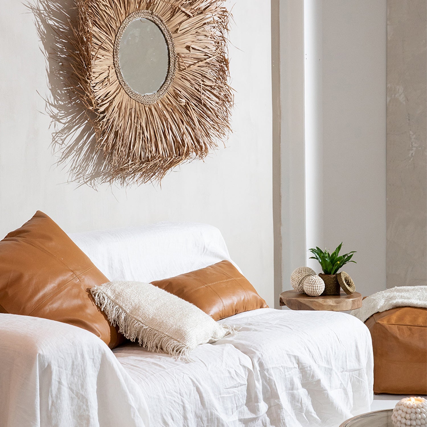 Stijlvolle woonkamer met witte bank, bruine kussens, rotan spiegel en plant op houten tafel voor serene sfeer.