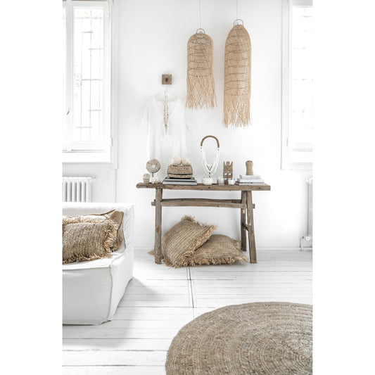 Lichte, rustieke kamer met houten tafel, geweven accessoires, hanglampen en beige kussen op witte vloer.