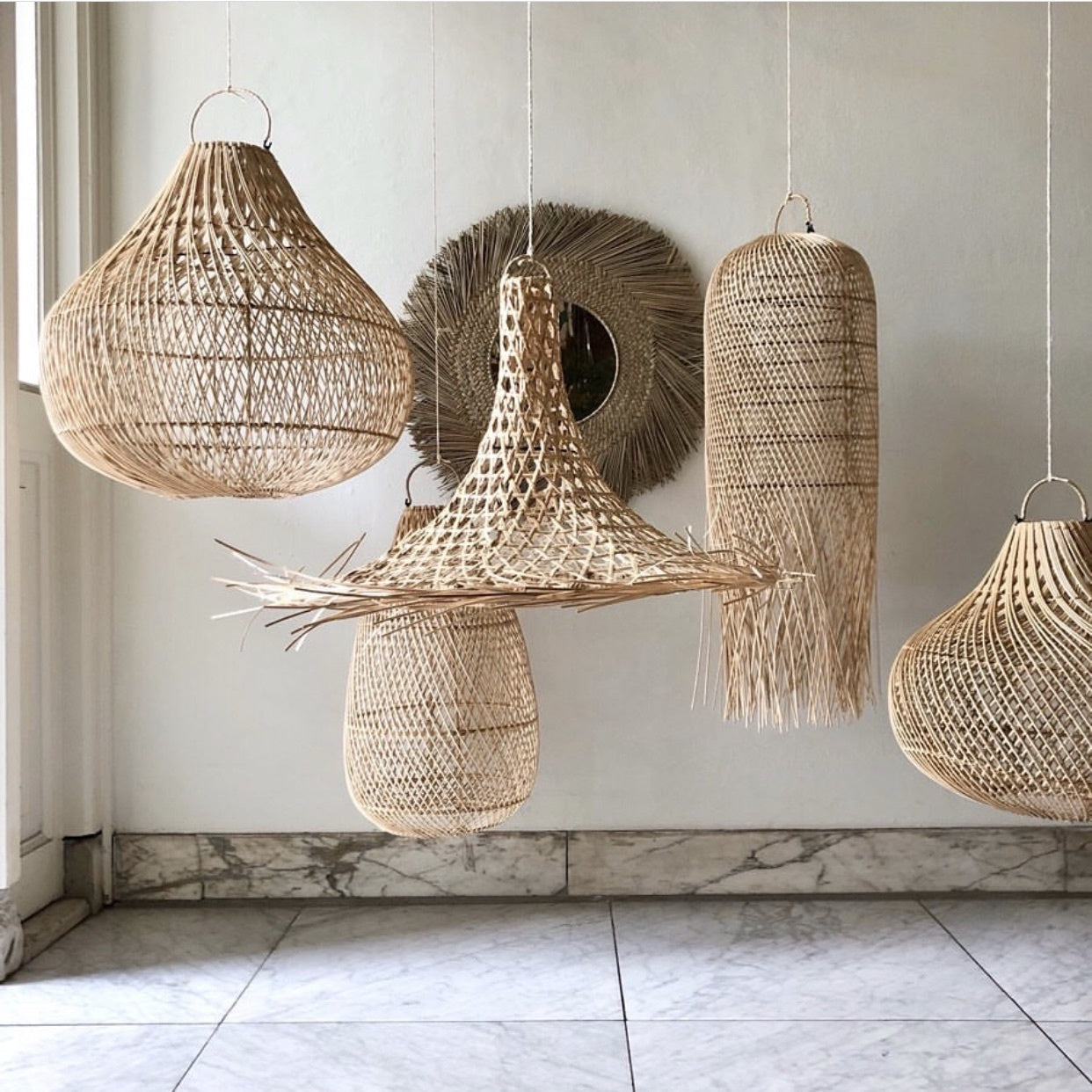 Gevlochten rotan hanglampen in diverse vormen hangen aan een plafond boven een marmeren vloer.