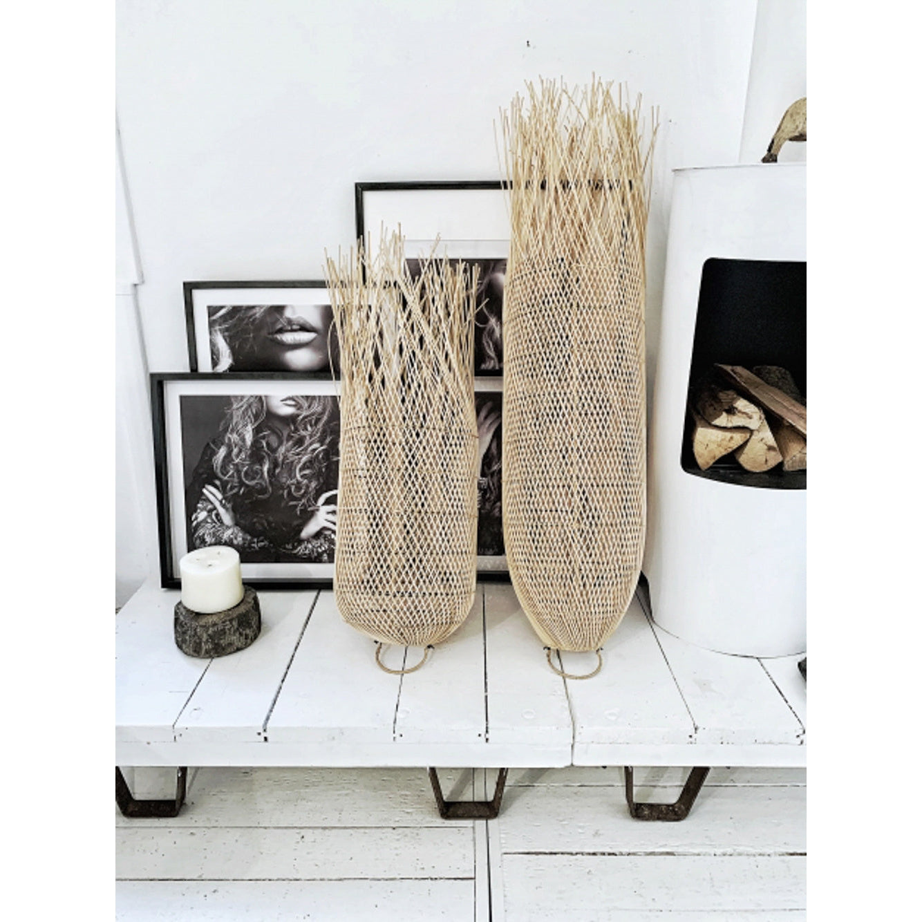 Twee geweven rieten decoratieve vazen voor zwart-wit portretten, naast een witte kachel op houten plank.