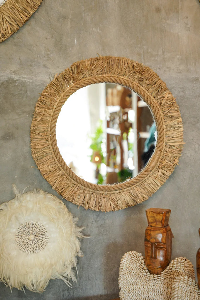 Ronde spiegel met gestoffeerde houten rand, witte decoratie en houten beeld op grijs betonnen muur.