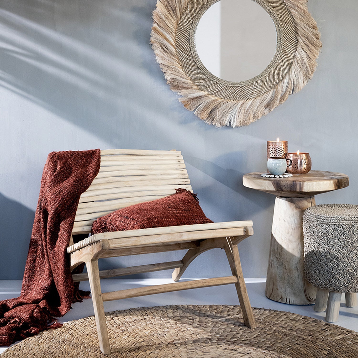 Houten stoel met roodbruine plaid, rieten spiegel en houten tafel met kaarsen in een rustieke kamer.