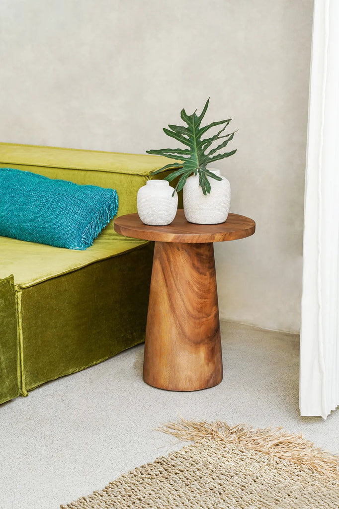 Houten bijzettafel met twee witte vazen en een groene plant, naast een olijfgroene bank en blauw kussen.