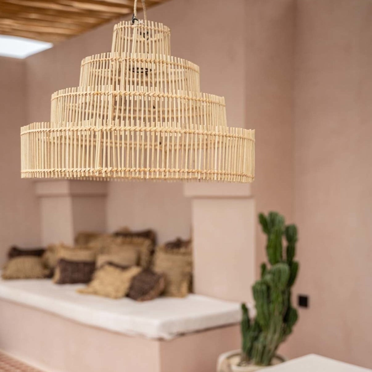 Rotan hanglamp boven een stijlvolle zithoek met kussens en een cactus op een beige achtergrond.