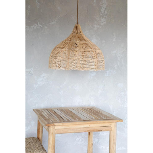 Hanglamp van rotan boven een houten tafel met rustieke afwerking, tegen een lichtgrijze gepleisterde muur.