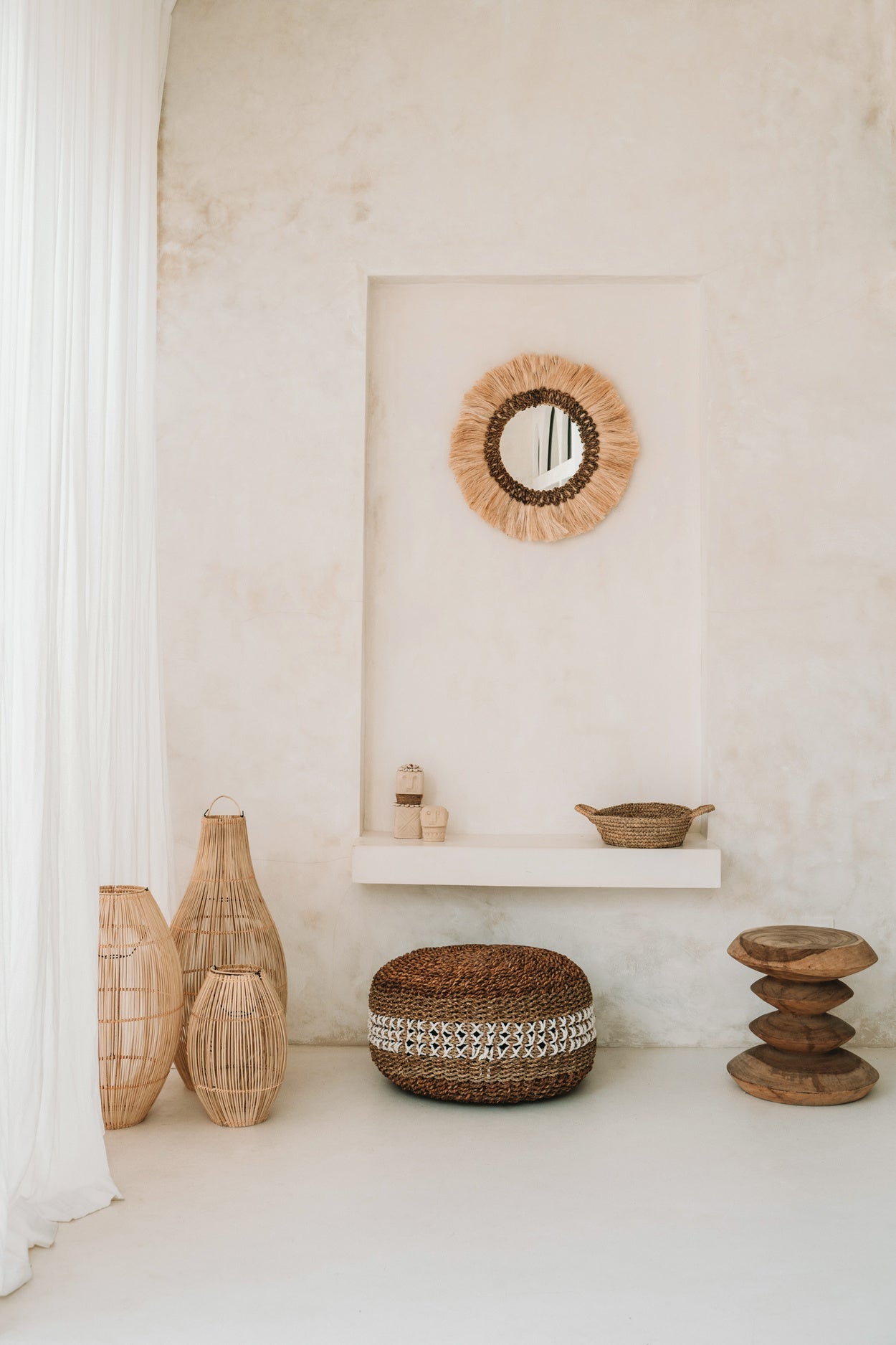 Rustieke minimalistische kamer met rieten objecten, boho spiegel, en houten accentstukken tegen witte muren.