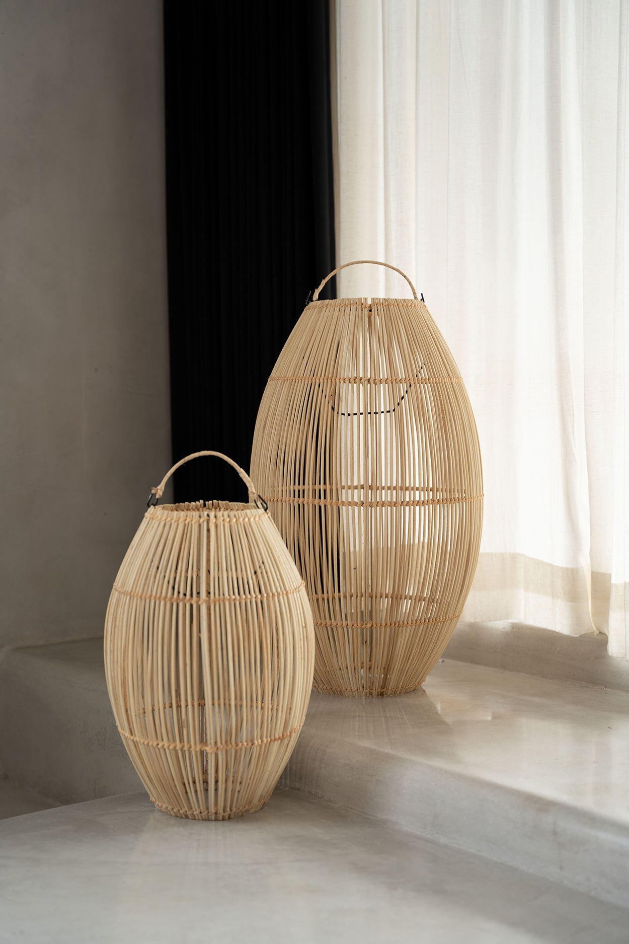 Twee grote rotan lampen in een minimalistische ruimte met zachte, natuurlijke verlichting en lichte gordijnen.