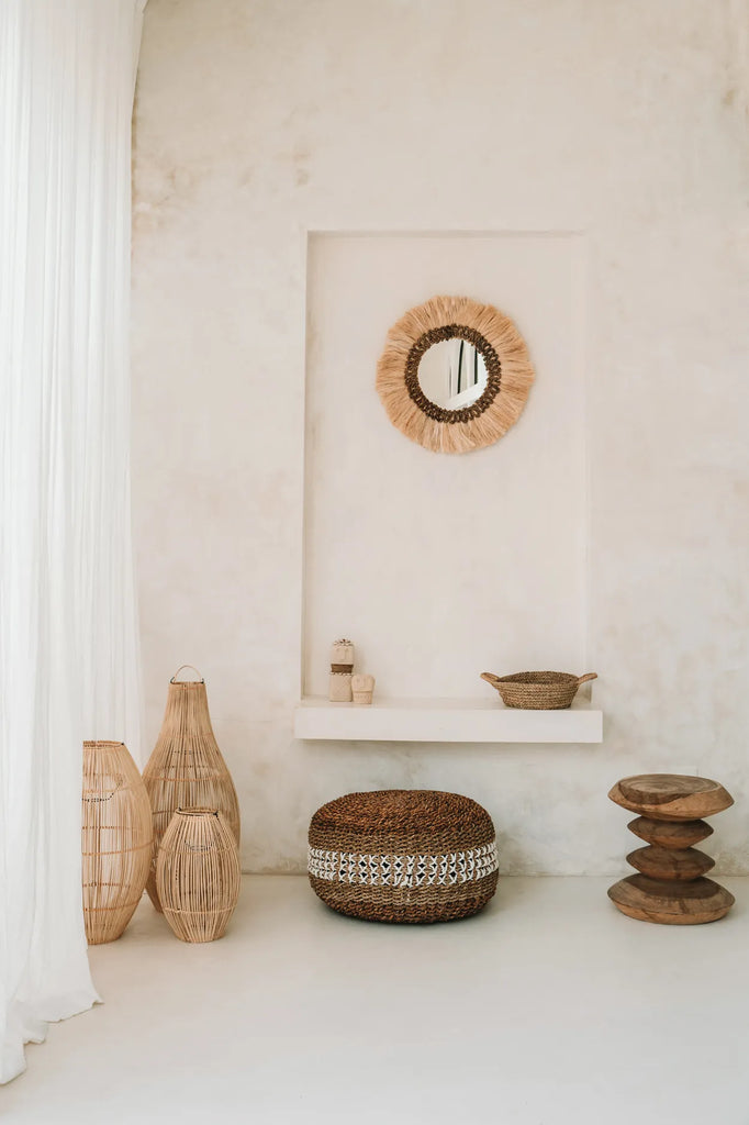 Stijlvolle minimalistische ruimte met natuurmaterialen: rieten manden, spiegel, kruk en decor tegen beige muur.