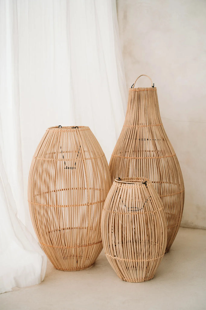 Drie elegante, natuurlijke rotan manden van verschillende grootte tegen een witte gordijnachtergrond.